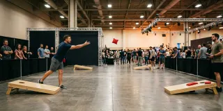 Players throwing bags down a cornhole lane on an indoor expo floor