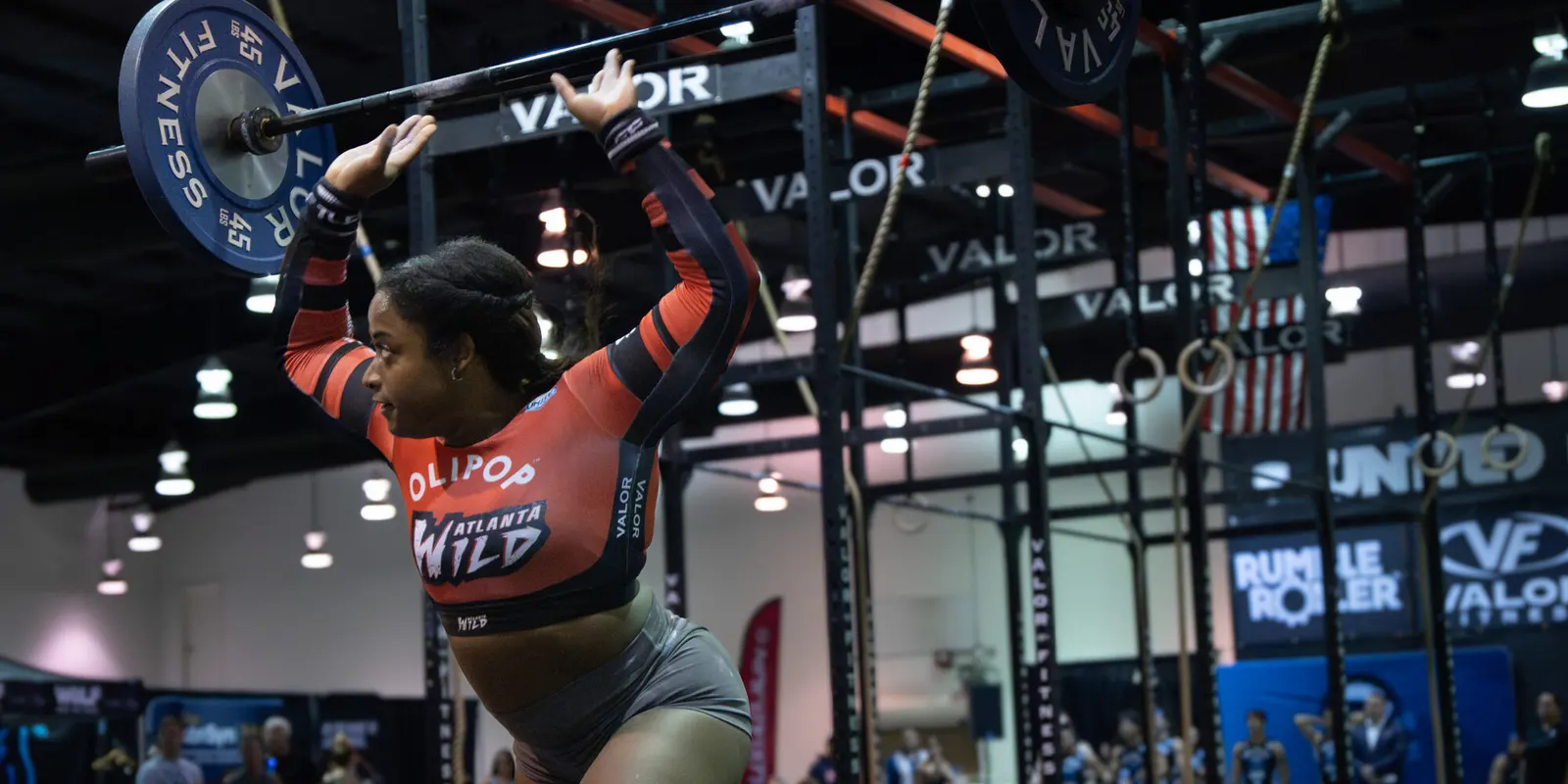 Sidney Wilson presses a barbell overhead in her red Atlanta Wild jersey during a Grid League match.